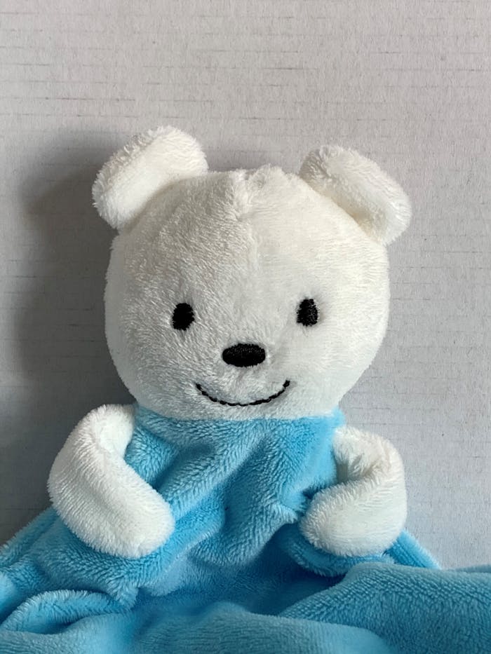 Cute white teddy bear with a soft blue blanket, perfect for kids' comfort.